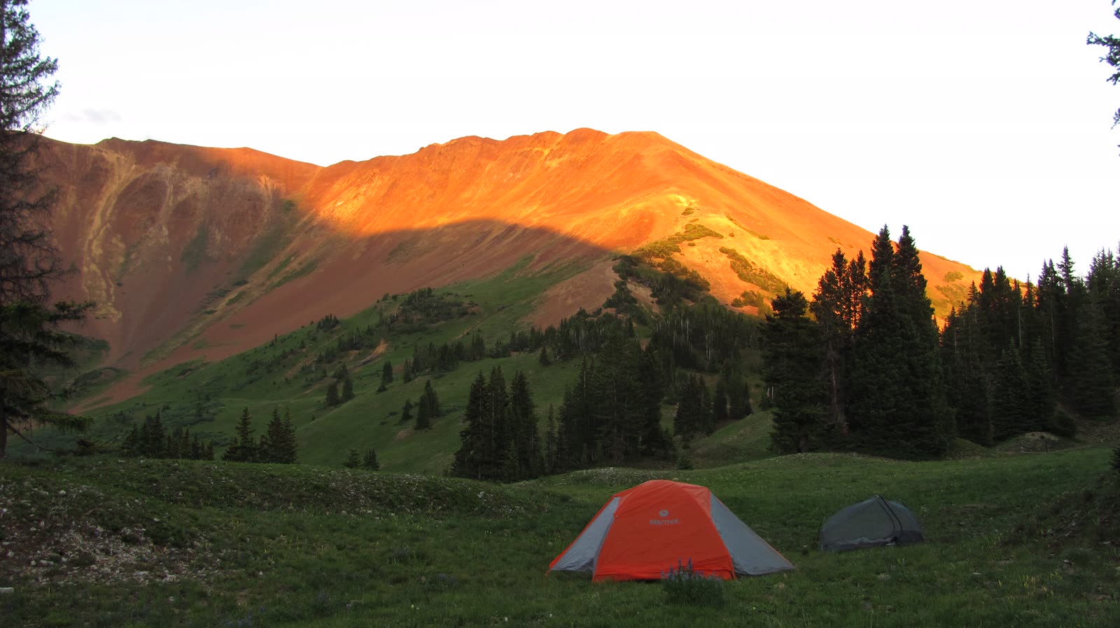 Two tents in a meadow below a ridge lit orange at sunset