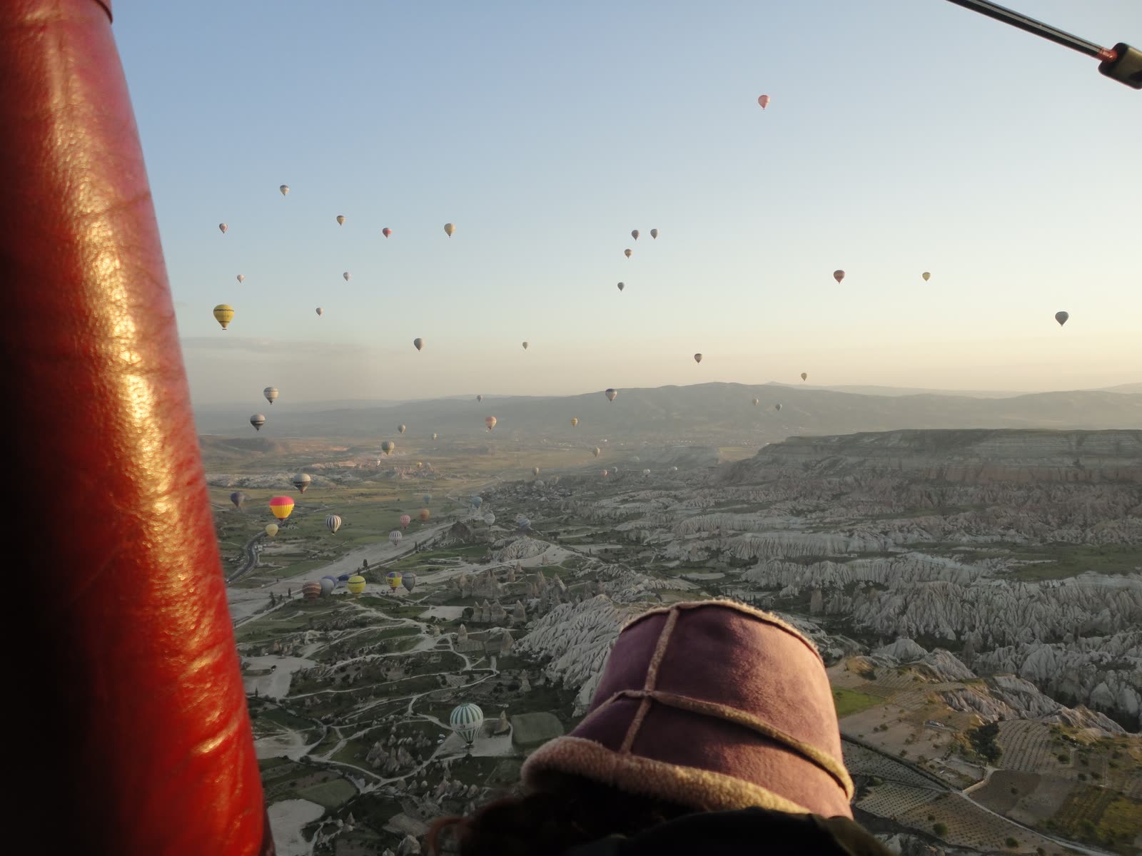 Hot air balloons drifting over a pale valley at dawn, shot from another balloon