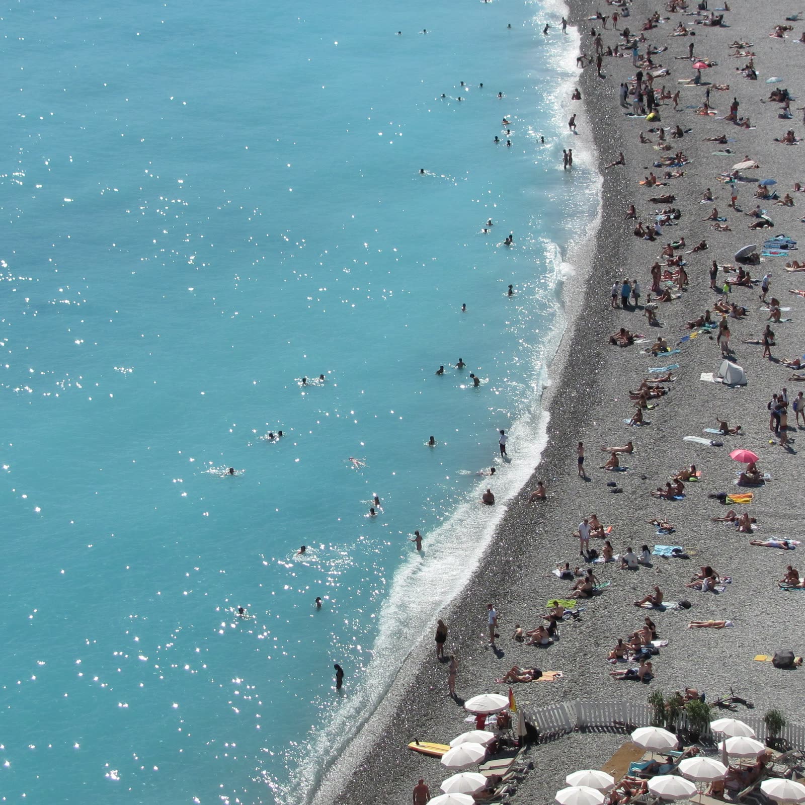 Crowded pebble beach curving along turquoise water, seen from above